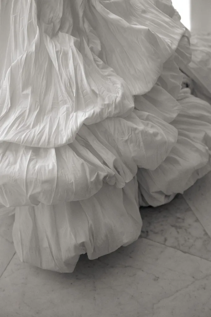 Black and white detail of a voluminous white gown with pleated tiers on marble