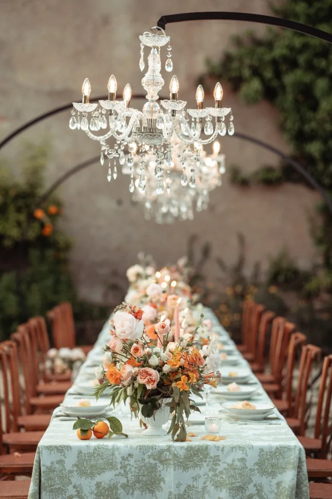 Real wedding at Casale Malatesta: outdoor banquet with mint toile de Jouy linen, peach and orange florals, citrus and crystal chandeliers against a stone wall