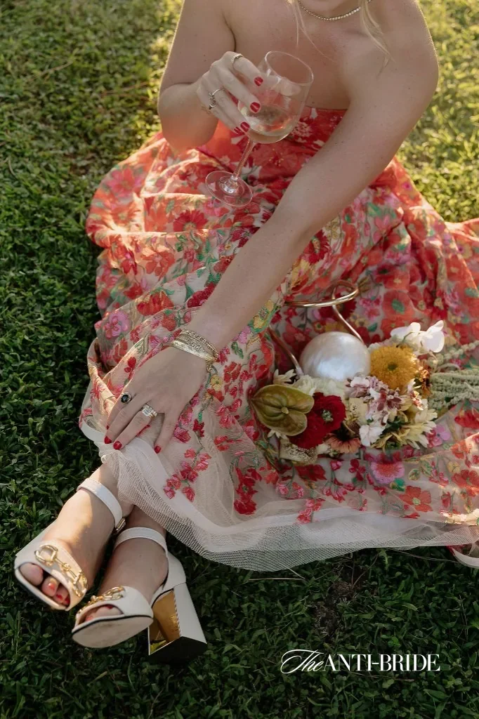 Sydney & Julien, Casale del Gallo, Rome: bride in floral skirt on the lawn with wine glass and bouquet detail