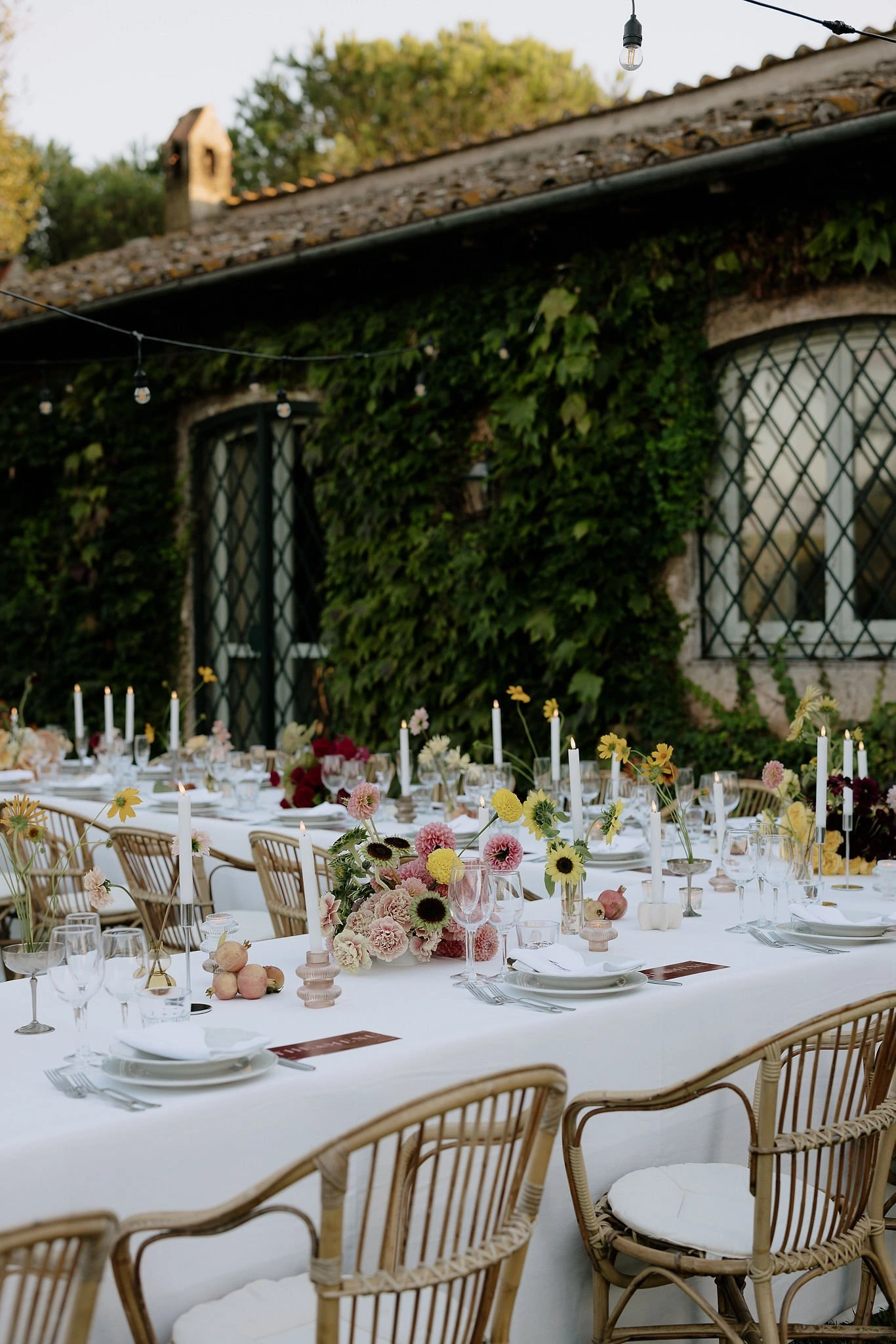 Long outdoor wedding reception table at a Roman villa, dressed with florals, candlelight and rattan chairs